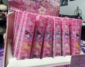May include: A pink and white display box filled with small pink and white boxes featuring various Sanrio characters. The boxes are labeled "QX6130 36PCS" and "Sanrio". The box is decorated with a pink and white checkered pattern and a floral design. The front of the box features a pink and white illustration of Hello Kitty and a white cow.