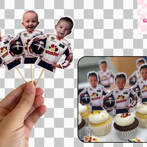 May include: Cupcake toppers depicting a baby in a racing suit, holding a helmet. The toppers are attached to wooden sticks. The image also shows cupcakes decorated with the toppers. The racing suit has the word "wonder".
