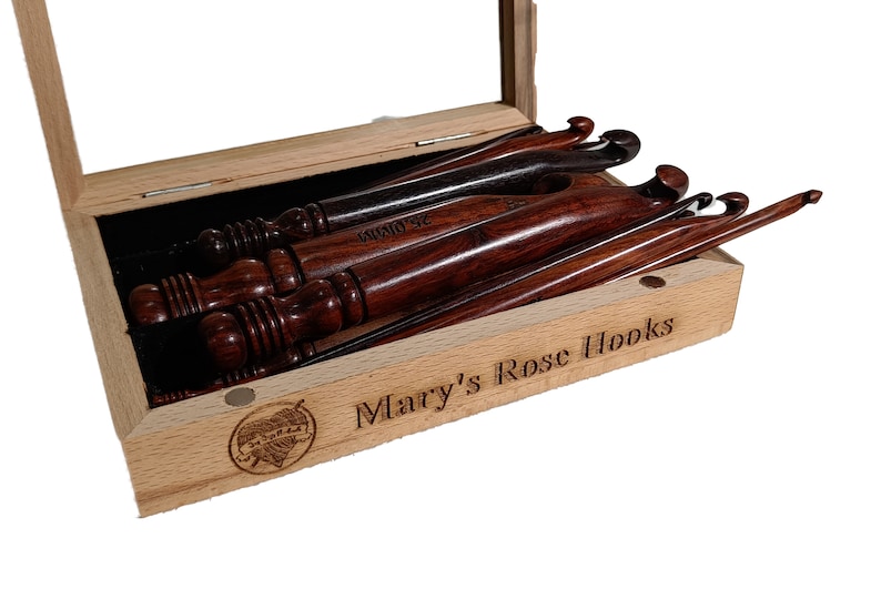 Op de afbeelding: Een set houten haaknaalden in een houten doos met een glazen deksel. De doos is gegraveerd met "Mary's Rose Hooks".