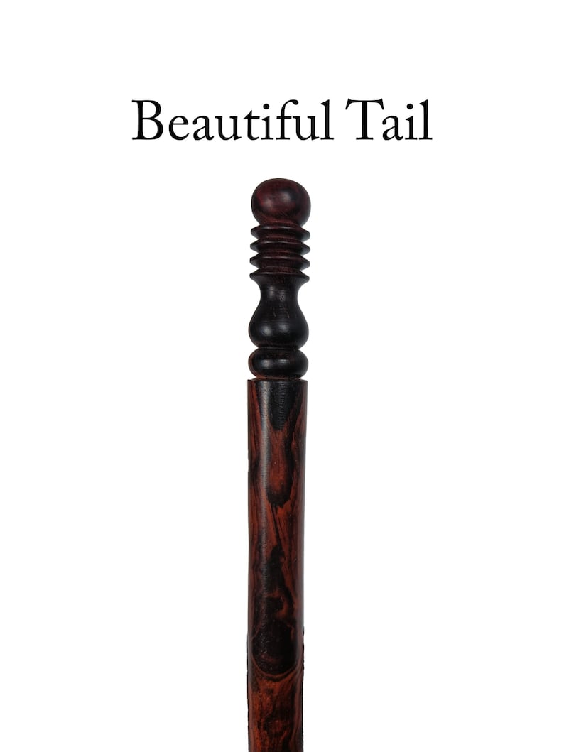 Op de afbeelding: Een houten wandelstok met een donkerbruin en rood houtnerfpatroon. De bovenkant van de stok heeft een donkerbruine knop met een decoratief ontwerp.