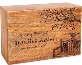 May include: A rectangular wooden cremation urn featuring a laser-engraved design of a park bench under a tree with a bird perched on the backrest. The text reads: in Loving Memory of Darrelle E. Arthur JULY 10, 1976 - AUGUST 4, 2023.