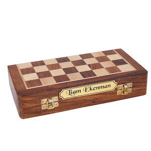 May include: A wooden chessboard set with a personalized brass plaque that reads "Liam Ekenman". The chessboard is closed and has brass clasps.