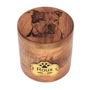 May include: A wooden pet urn with a laser engraved image of a dog and a brass plaque with the name "Roux" and the dates "2004 - 2024".