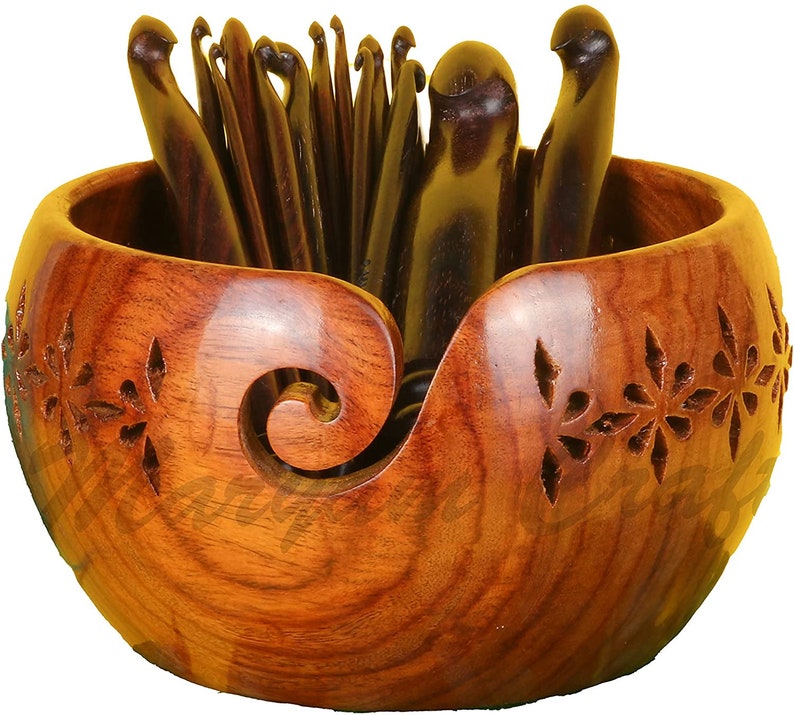 Op de afbeelding: Een houten garenkom met een gesneden bloemenpatroon en een ingebouwde garengeleider. De kom is gevuld met een set houten haaknaalden.