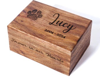 May include: A wooden pet urn with a paw print and the inscription "Lucy 2004-2024 Forever in our Hearts".