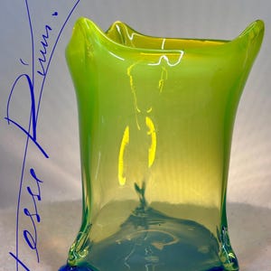 May include: A colourful, hand-blown glass vase with a distinctive, flared form. The vase displays a gradient of colours, shifting from a bright green at the top to a deep blue at the base. The text "Tesserium" is visible at the bottom.