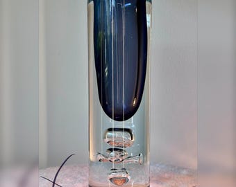 Könnte beinhalten: Eine zylindrische Glasvase mit einem tiefblauen Innenkern, der von klarem Glas umschlossen ist. Der Boden enthält drei deutlich sichtbare, vertikal gestapelte Luftblasen. Am Boden ist der Text "CZECH REPUBLIC" eingraviert.