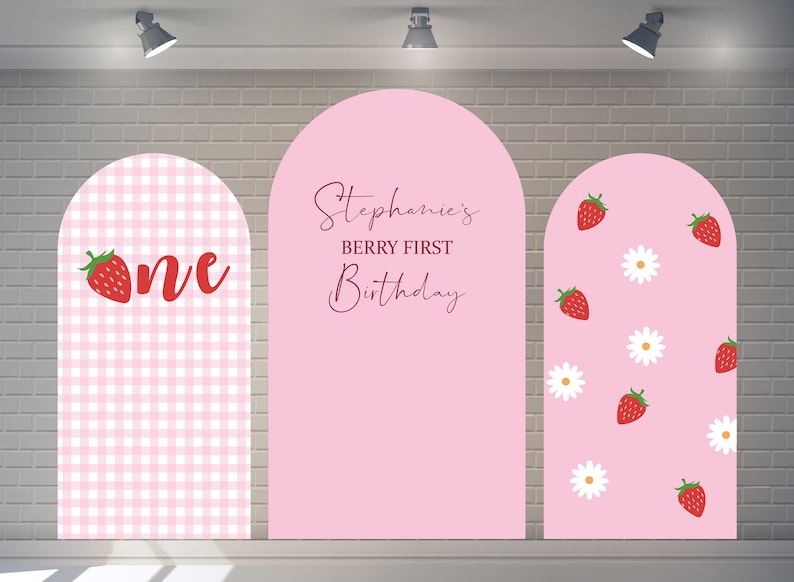 May include: Three pink arch backdrops for a first birthday party. The left backdrop has a pink and white gingham pattern with a red strawberry and the word "one". The middle backdrop has the text "Stephanie's Berry First Birthday". The right backdrop has a pink background with white daisies and red strawberries.