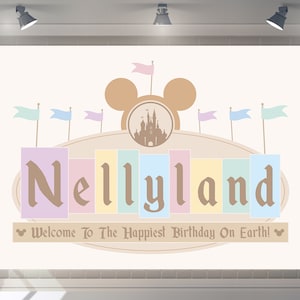May include: A pastel-coloured sign with the text "Nellyland" in brown lettering. The sign features a Mickey Mouse silhouette with a castle inside. The text "Welcome to the Happiest Birthday on Earth!" is below the sign.