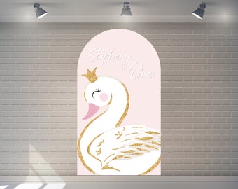 May include: Pink and gold arch backdrop with a white swan with a gold crown and the text "Stephanie is One".