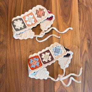 Two handmade crochet granny square headbands laid flat on a wooden surface, featuring floral square motifs in neutral and earthy tones with adjustable ties.