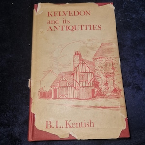 Puede incluir: Un libro antiguo titulado "Kelvedon and its Antiquities" con una cubierta roja y una sobrecubierta beige. La portada presenta una ilustración roja de edificios y el nombre del autor, B.L. Kentish. El libro muestra signos de desgaste.