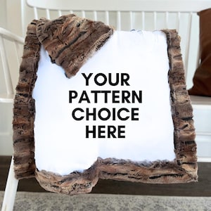 May include: A plush blanket with a white center and a brown, textured border. The blanket is draped over a white chair. The text "YOUR PATTERN CHOICE HERE" is printed in black on the white center.
