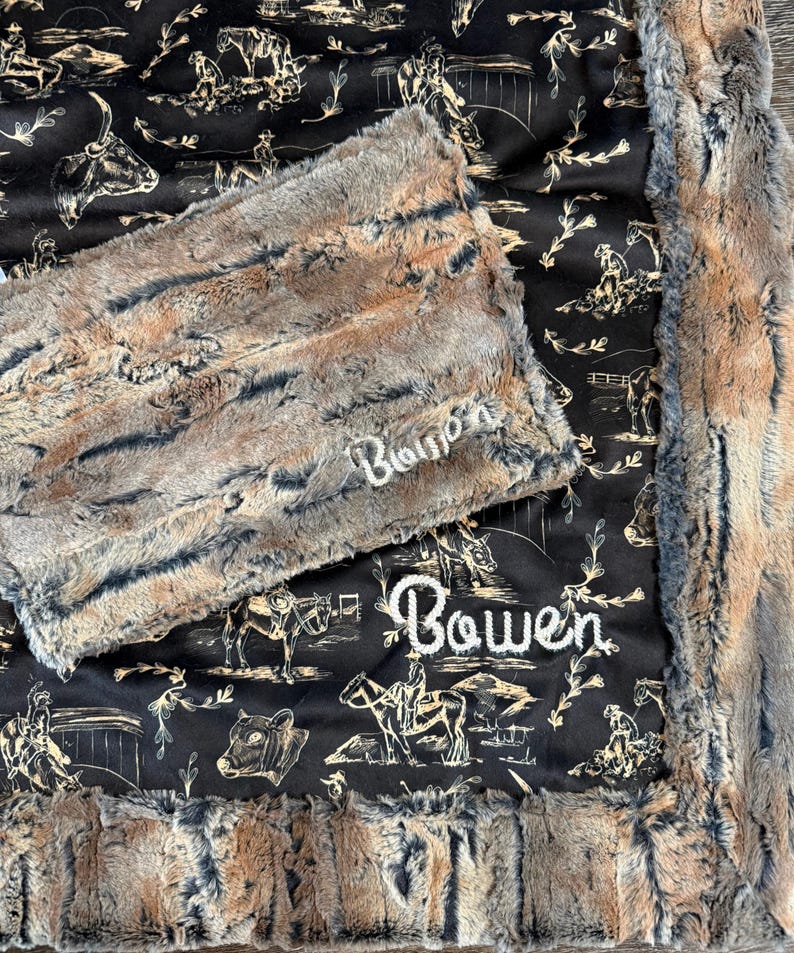 Puede incluir: Una manta de felpa de piel sint&eacute;tica con un patr&oacute;n marr&oacute;n y gris, con el nombre "Bowen" bordado en blanco. El reverso de la manta es negro con un estampado crema de tem&aacute;tica occidental de vaqueros, caballos y ganado.