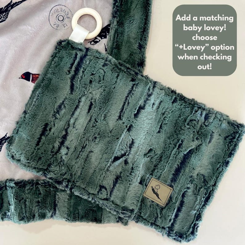 May include: A green plush baby blanket with a pheasant design. The blanket has a matching lovey with a wooden ring attached.