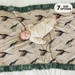 May include: A baby lying on a beige and green plush blanket with a pheasant print. The blanket has a green faux fur trim. The text "7 SIZE OPTIONS" is in the upper right corner of the image.