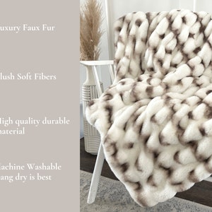 May include: A white and brown faux fur throw blanket draped over a white chair. The blanket has a woven design with plush, soft fibers. The image also includes text that says "Luxury Faux Fur", "Plush Soft Fibers", "High quality durable material", and "Machine Washable Hang dry is best".