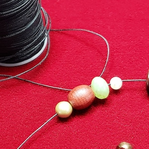 May include: A close-up of a necklace with various beads, including brown, red, white, and gold beads. The necklace is on a red surface.