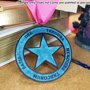 Op de afbeelding: Een ronde, houten, blauwe en zwarte stervormige medaille met de woorden "TREGUNA MEKOIDES TRECORUM SATIS DEE" rondom de rand.