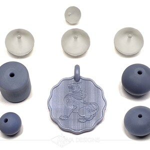 May include: A set of gray and white beads and a pendant featuring a detailed engraving of a mythical creature. The pendant is silver in color and has a textured surface. The beads are various shapes and sizes, including round, cylindrical, and flat.