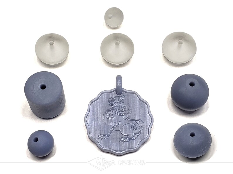 May include: A set of gray and white beads and a pendant featuring a detailed engraving of a mythical creature. The pendant is silver in color and has a textured surface. The beads are various shapes and sizes, including round, cylindrical, and flat.