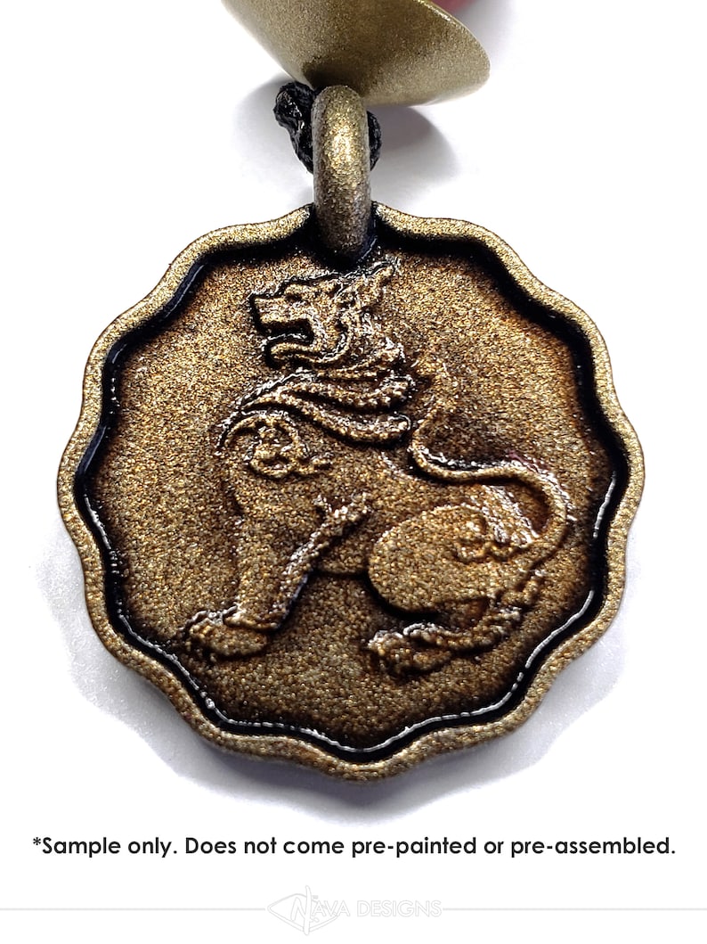 May include: A circular, scalloped-edge pendant featuring a raised relief of a seated lion. The piece has a textured, metallic bronze finish. Below the pendant, the text reads: *Sample only. Does not come pre-painted or pre-assembled. NAVA DESIGNS.