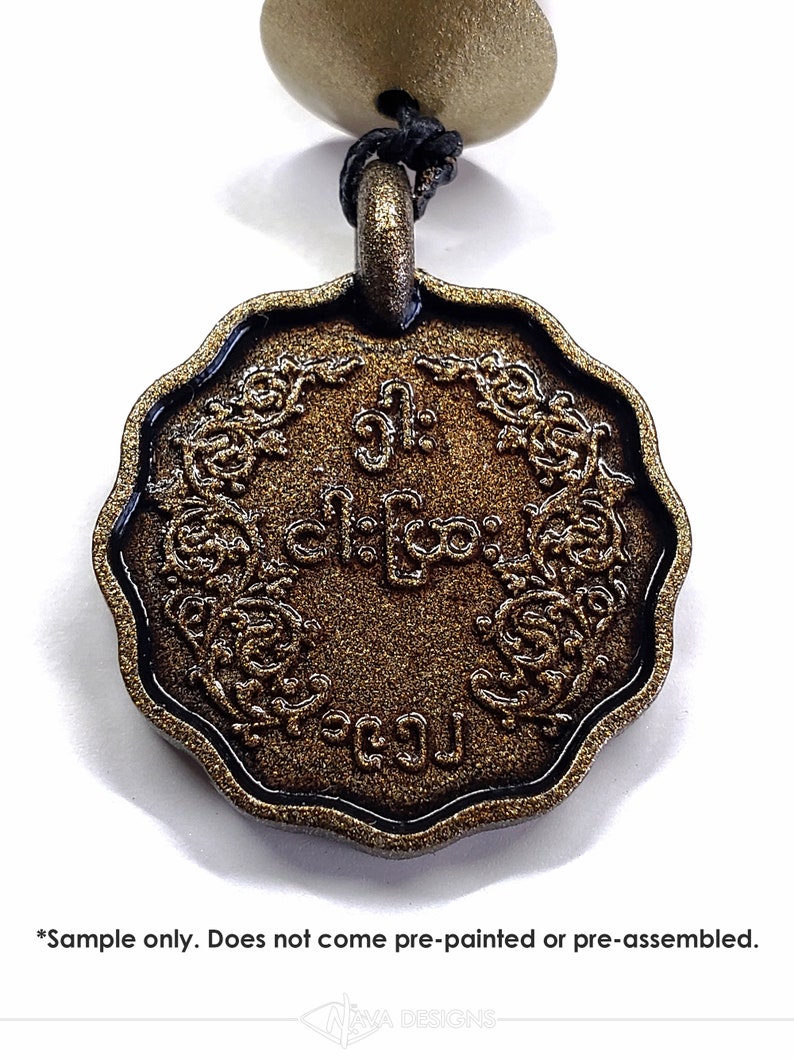 May include: A circular bronze-colored pendant with a scalloped edge and a textured surface. The center features embossed script characters surrounded by an intricate floral border. A black cord passes through a loop at the top of the pendant.