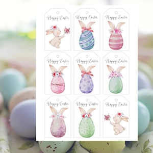 Peut inclure: Neuf étiquettes cadeaux de Pâques blanches avec des illustrations à l'aquarelle de lapins et d'œufs décorés. Chaque étiquette porte l'inscription "Joyeuses Pâques" en écriture noire. Les étiquettes sont sur fond blanc, avec des œufs de Pâques pastel flous en arrière-plan.