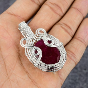 Pode incluir: Um pingente de fio de prata com uma grande gema de cor vermelha escura de forma oval.