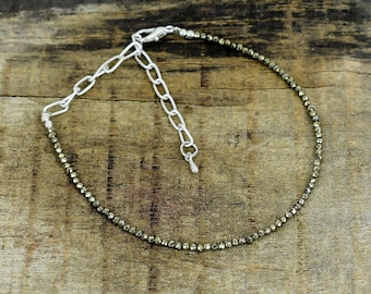 May include: A delicate bracelet featuring a single strand of small, faceted metallic pyrite beads. The bracelet includes a silver-toned metal chain extender with oval links and a small, smooth teardrop-shaped charm at the end of the adjustment chain.
