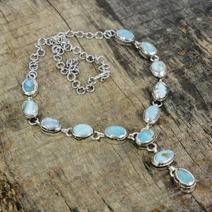 Puede incluir: Un collar de plata con un colgante de piedra azul. El collar está hecho de una cadena con piedras ovaladas.