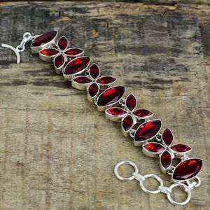 May include: A silver bracelet featuring a series of oval and petal-shaped, deep red gemstones. The gemstones are set in a silver metal, creating a floral pattern. The bracelet has a toggle clasp.