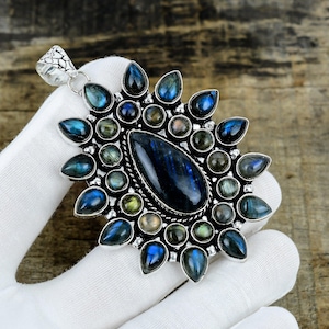 May include: A silver pendant featuring a large central pear-shaped labradorite gemstone surrounded by multiple smaller round and teardrop-shaped labradorite stones. The metal setting has a decorative rope-like border and a textured bail at the top.