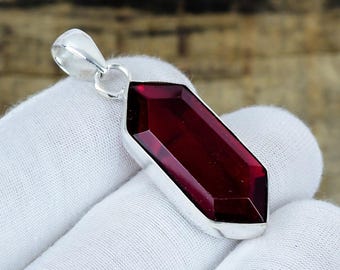May include: A faceted, deep red, hexagonal gemstone pendant set in a polished silver-toned metal frame. The pendant features a pointed, elongated shape with a smooth, reflective surface and a silver-toned bail at the top for attachment to a chain.