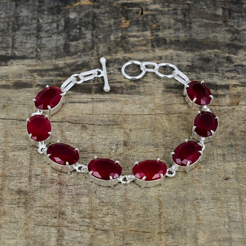 May include: A silver bracelet with a toggle clasp features seven oval-shaped red gemstones.