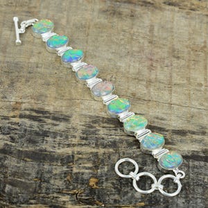 May include: A silver bracelet featuring oval-shaped opals in shades of green, blue, and pink. The opals are set in individual silver bezels and connected by silver links. The bracelet has a toggle clasp.