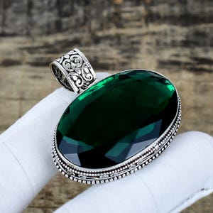 Puede incluir: Colgante de plata con una piedra preciosa ovalada de color verde esmeralda. El colgante tiene una fianza adornada y un borde detallado con cuentas. La piedra está engastada en un bisel de plata.