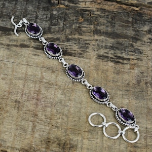 Peut inclure: Un bracelet en argent orné de pierres précieuses ovales de couleur violette. Les pierres sont serties dans un cadre perlé et reliées par des maillons en argent. Le bracelet a un fermoir à crochet et trois anneaux de connexion.