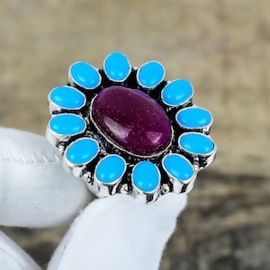 May include: A silver ring with a large purple gemstone surrounded by a ring of smaller turquoise gemstones.