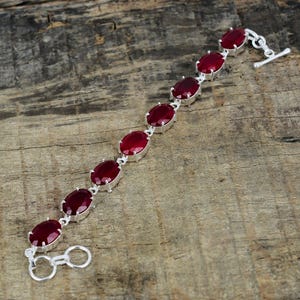 May include: A silver bracelet with seven oval-shaped red gemstones. The bracelet has a lobster clasp closure.