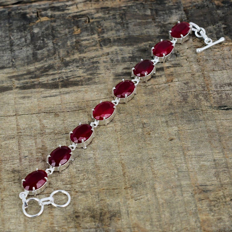 May include: A silver bracelet with seven oval-shaped red gemstones. The bracelet has a lobster clasp closure.