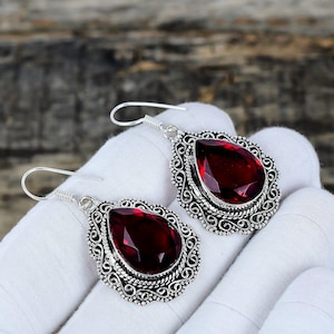 Può includere: Un paio di orecchini in argento con pietre preziose rosso scuro a forma di goccia. Gli orecchini presentano un design a filigrana ornato attorno alle pietre preziose e una semplice chiusura a gancio.