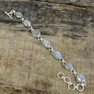 Puede incluir: Una pulsera de plata con piedras preciosas ovales de color azul pálido. La pulsera está conectada por eslabones de plata y tiene un cierre de palanca. Las piedras están engastadas en biseles de plata, creando un diseño delicado.
