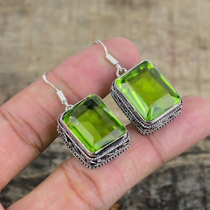 Puede incluir: Un par de pendientes de plata con gotas de piedras preciosas verdes. Los pendientes tienen un diseño de filigrana alrededor de las piedras.