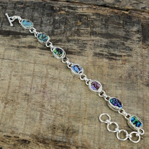 May include: A silver bracelet with oval-shaped abalone shell accents. The bracelet has a lobster claw clasp and a silver chain.