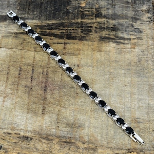 May include: A silver-toned metal bracelet featuring a repeating pattern of oval-cut black stones alternating with small, clear, round-cut stones. The bracelet includes a secure metal clasp at one end and a hinged connector at the other end.