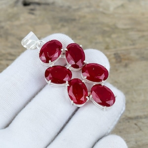 May include: A silver pendant with seven oval, deep red gemstones. The gemstones are arranged in a cascading cluster design, with a silver bail at the top for a chain. The pendant is displayed against a white background.
