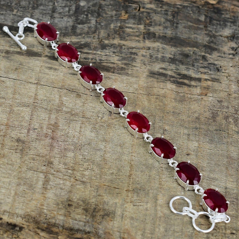 May include: A silver bracelet with a clasp closure features a row of oval-shaped red gemstones.