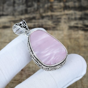 May include: A silver pendant featuring a pear-shaped, pale pink stone with a swirling pattern. The stone is set in a detailed silver frame. The pendant has a decorative bail for a chain.
