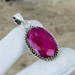 Puede incluir: Colgante de plata con una gran gema de rubí ovalada. El rubí, de un vibrante color magenta, está engastado en un marco de plata decorativo con un diseño de cuerda trenzada. El colgante tiene una argolla de plata. El rubí mide unos 2,5 cm de largo.